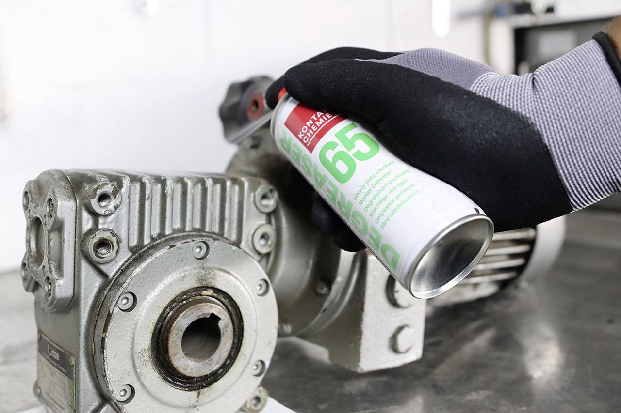 Ruka v čiernej rukavici strieká mazivo z dózy na kovový strojný diel.