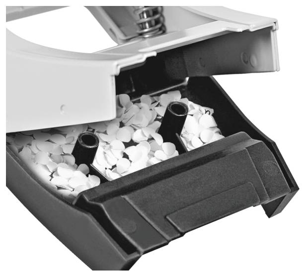 Otvorená zásuvka dierkovača so zachytenými bielymi papierovými konfetami na čiernom pozadí.