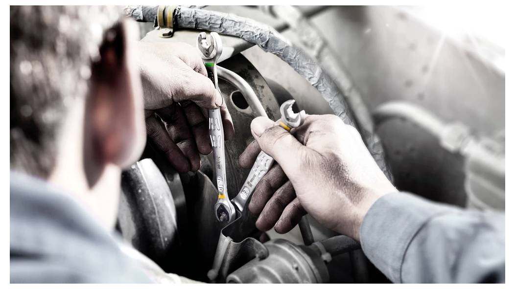 Mechanik používajúci kľúče na opravu komponentov motora v motorovom priestore automobilu.