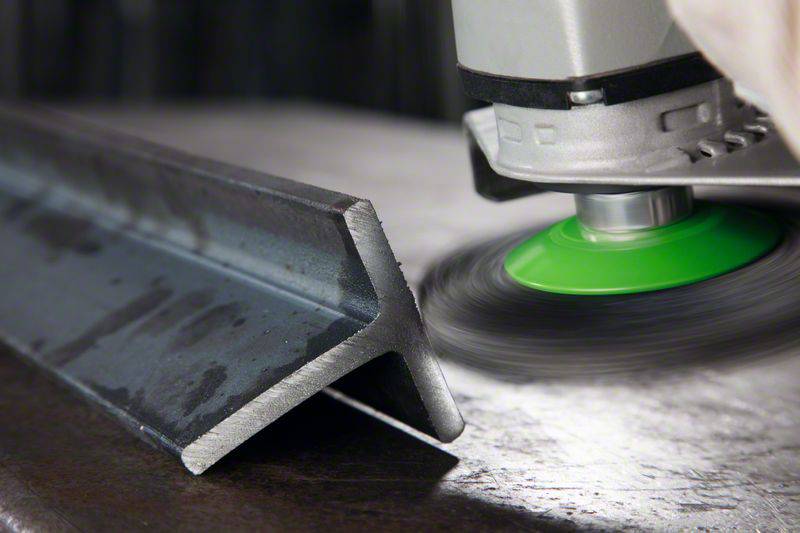 Kovový brúsič leští hranu L-profilového oceľového dielu, vytvára iskry a hladký povrch. Ruka robotníka je viditeľná.