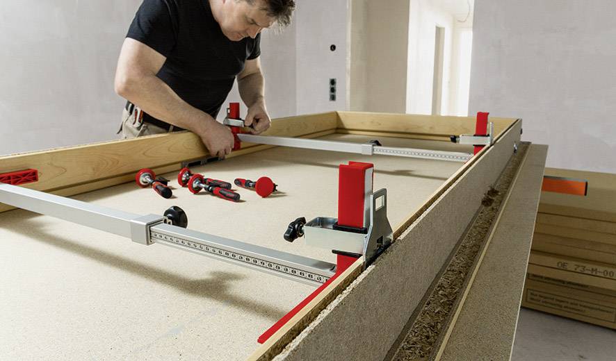 Muž montuje drevené dosky pomocou kovového nástroja na stole.