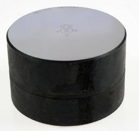 Kruhový kremíkový wafer, hladký a sivý, umiestnený na tmavom valcovitom podstavci.