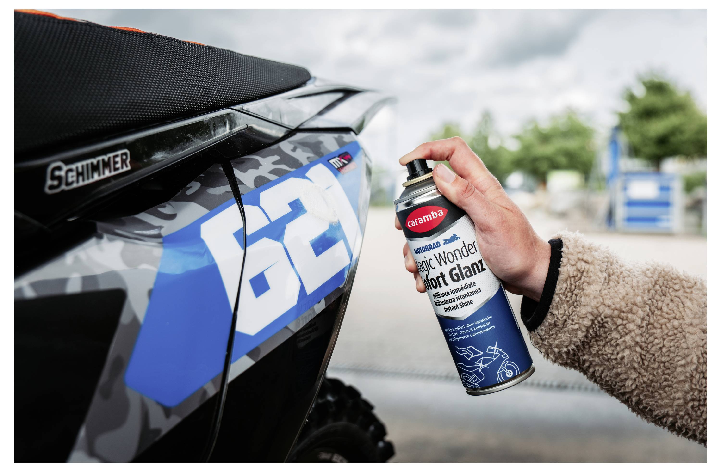 Sprej na ruky 'Muc-Off' 'Silk Matt Finish' na modrom paneli s číslom 62 na dirtbike vedľa sedla 'Schimmer'.