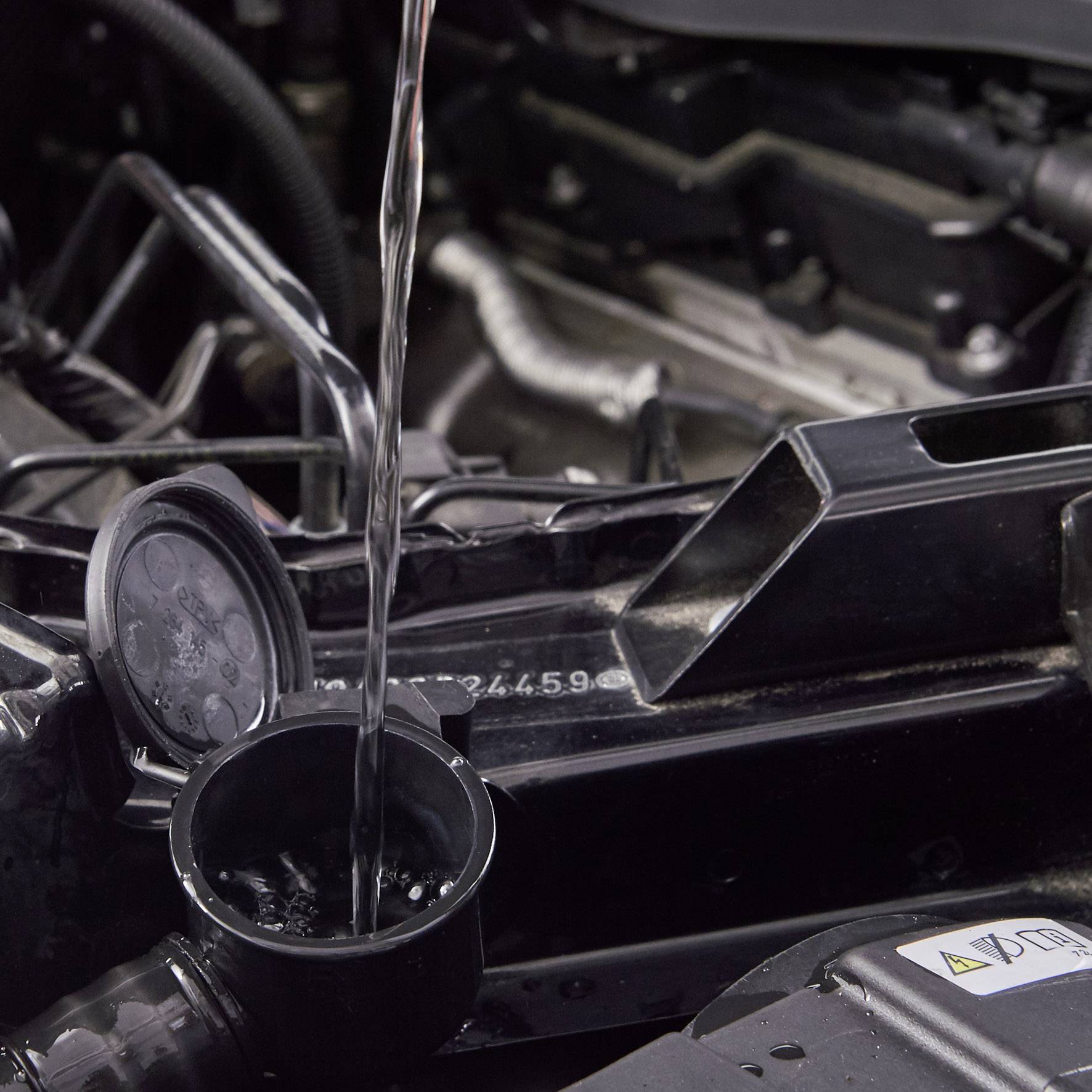 Motorový olej sa nalieва do automobilového motora. Otvorený uzáver oleja leží vedľa. Dôraz je kladený na dopĺňanie oleja.