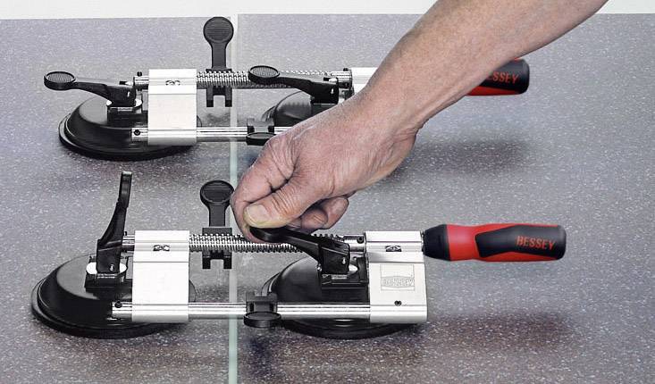Jedna ruka nastavuje nivelačný nástroj na obkladačky s dvoma prísavkami na hladkom povrchu, aby vyrovnala dlaždice.