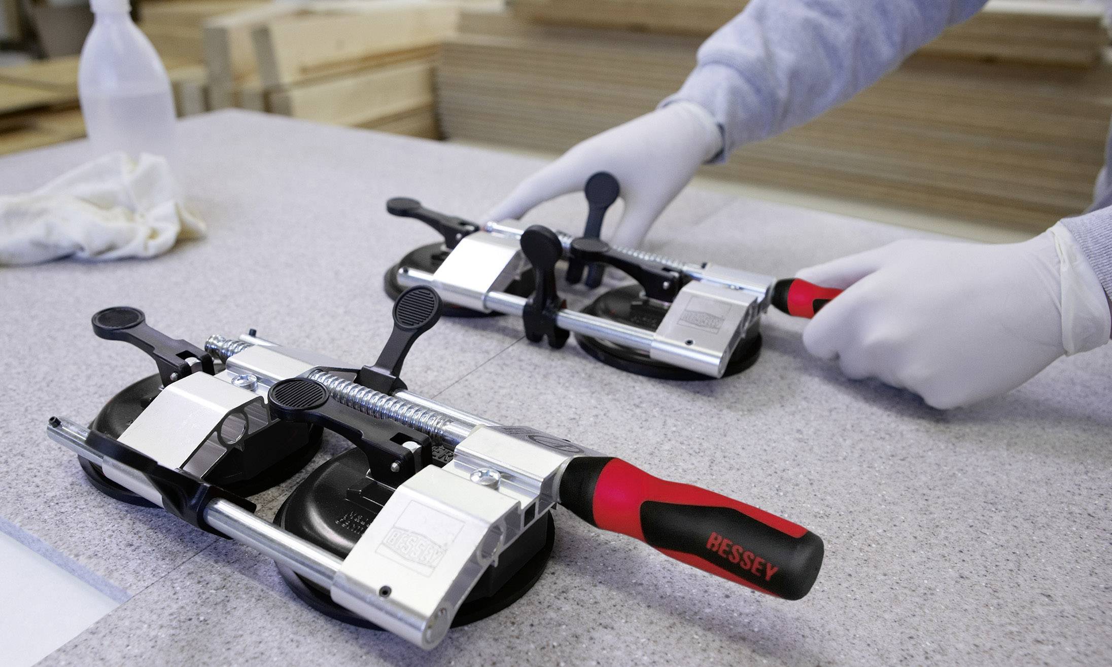 Osoba v rukaviciach drží dva vákuové prísavky Bessey, pripravená na zdvíhanie a prepravu plôch.