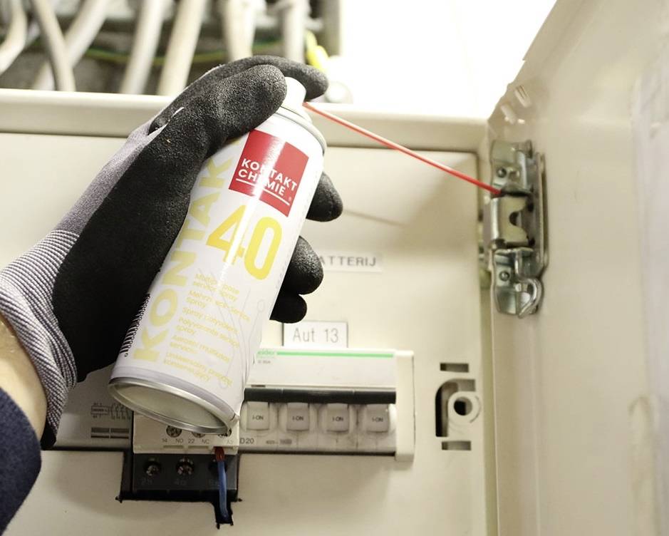 Osoba v rukaviciach strieká mazivo na záves elektrického rozvádzača.