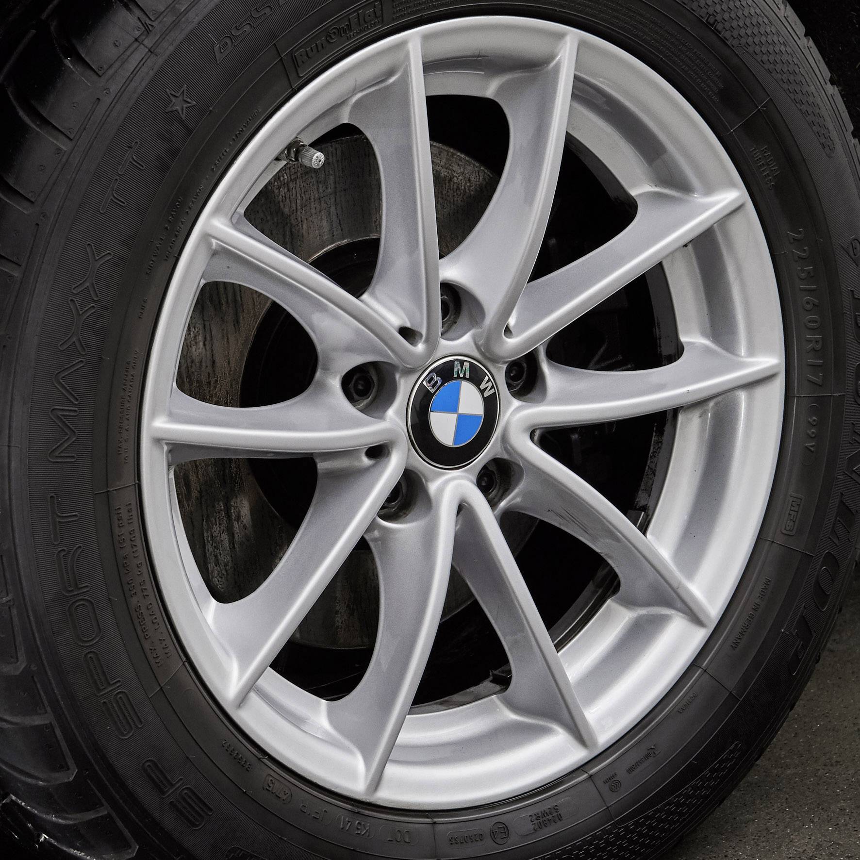 Detailný záber strieborného pneumatiky automobilu BMW s modro-bielym logom na ráfiku, nainštalovaný na vozidle.