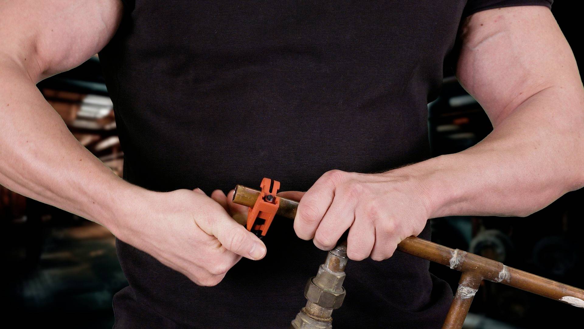 Osoba v čiernom tričku strihá medené potrubie rezačom rúr v prostredí dielne.
