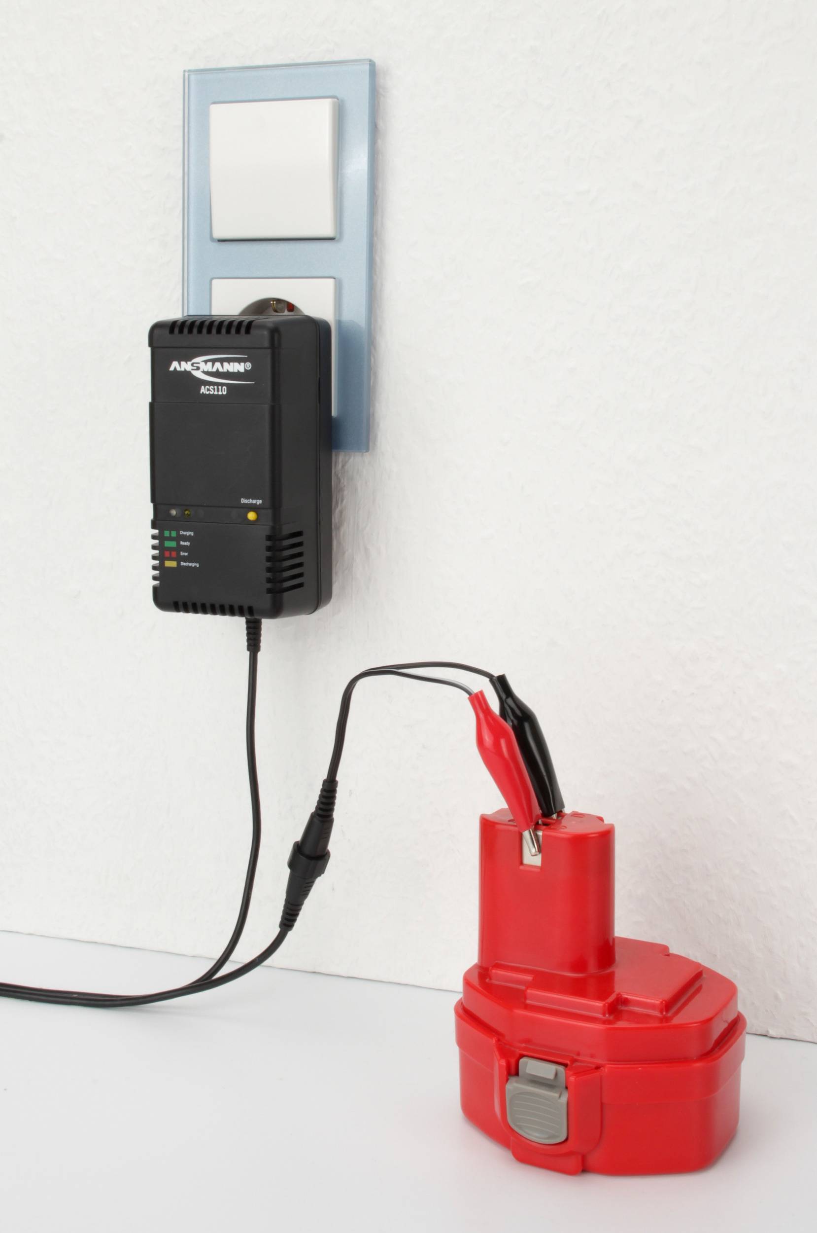 Červený akumulátor je pripojený k nabíjačke cez elektrickú zásuvku. Nabíjačka zobrazuje stav nabíjania pomocou LED diódy.