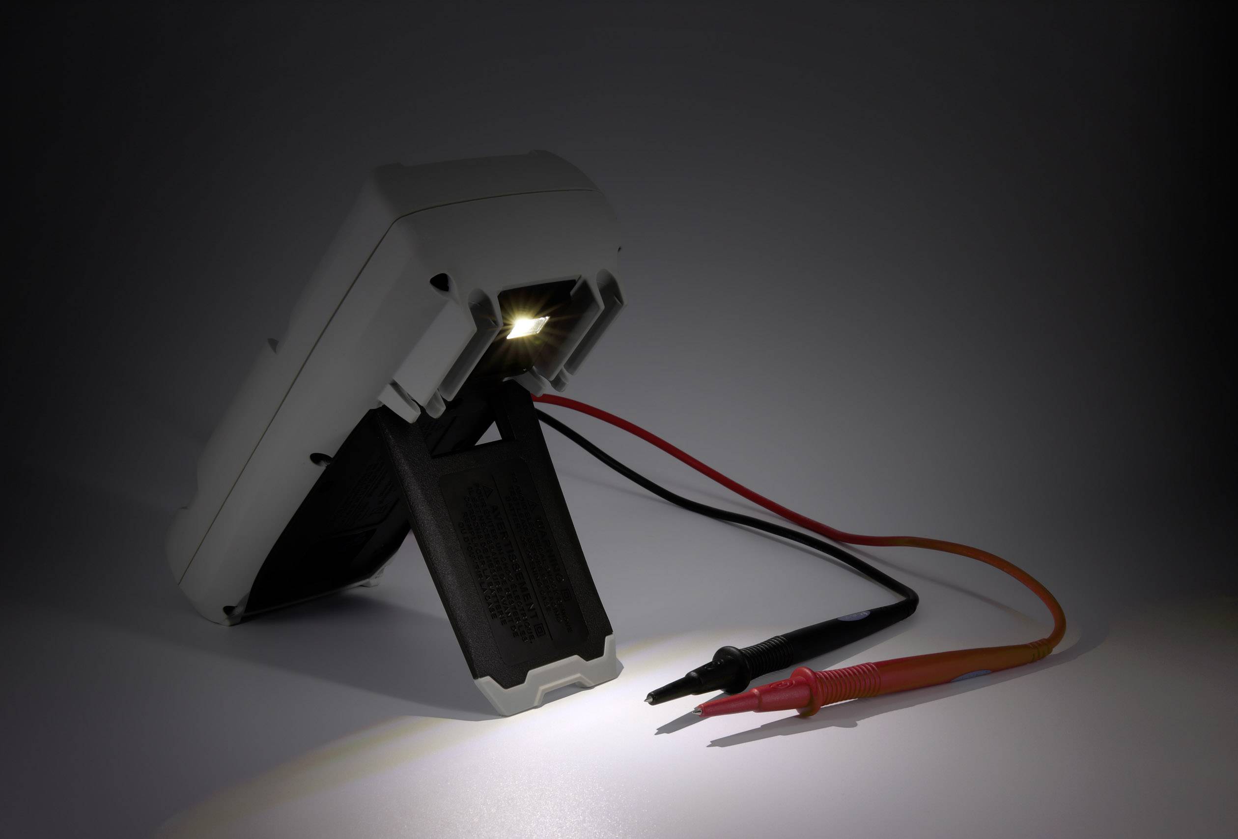 Digitálny multimeter zobrazuje rozsah displeja a meracie vodiče pripojené k prístroju s podsvietením.