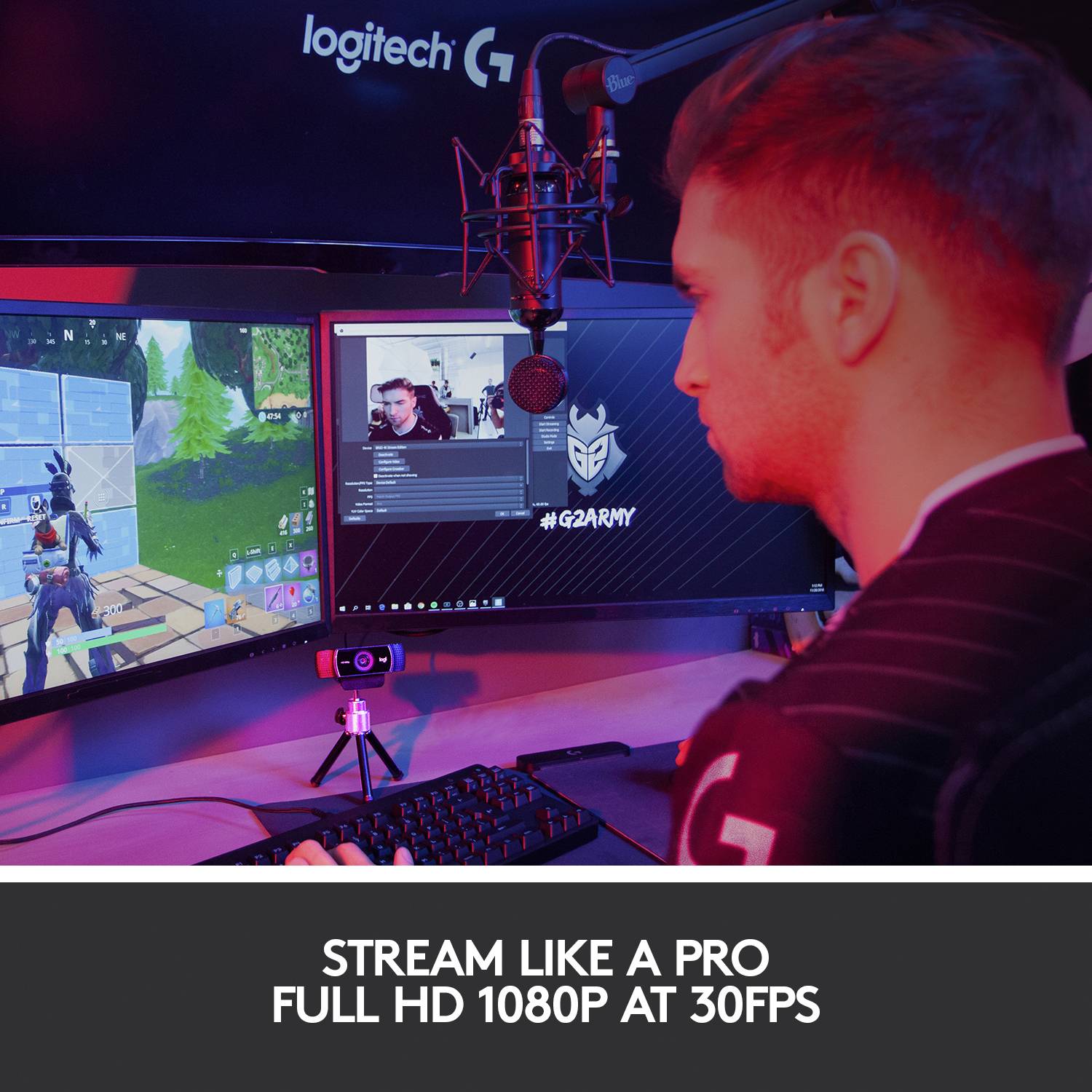 Muž sedí pri pracovnom stole a streamuje videohru na dvoch monitoroch. Hore je mikrofón; scéna pôsobí profesionálne.