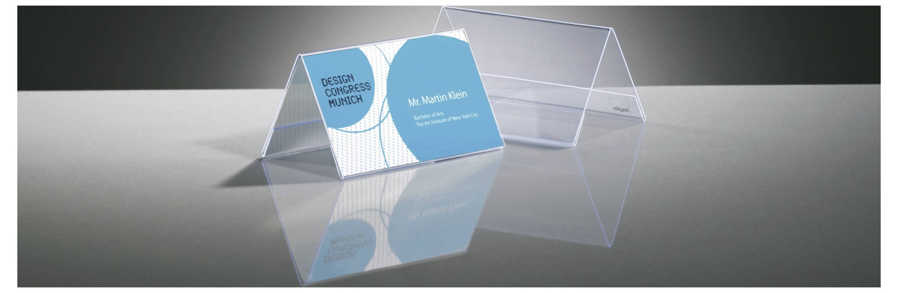 Transparentný akrylový stojan na vizitky zobrazujúci modrú vizitku "Dazzle Custom Graphics" pre pána Martina Kleina na reflektívnom sivom povrchu.