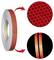 Rolka červenej reflexnej pásky s zväčšenými pohľadmi zobrazujúcimi bezpečnostný vzor vo fáze a reflexný pás na tmavom povrchu.