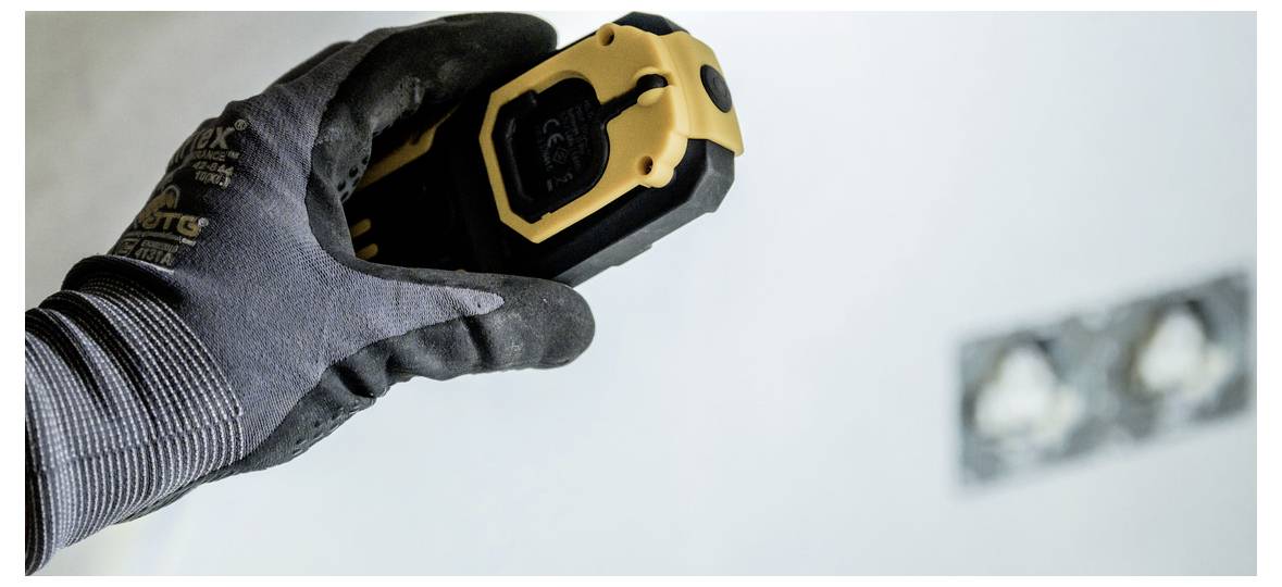 Rukavica ruky držiaca žltý laserový diaľkomer zameraný na stenu, čo naznačuje meracie alebo rozmetávacie práce počas renovácie.