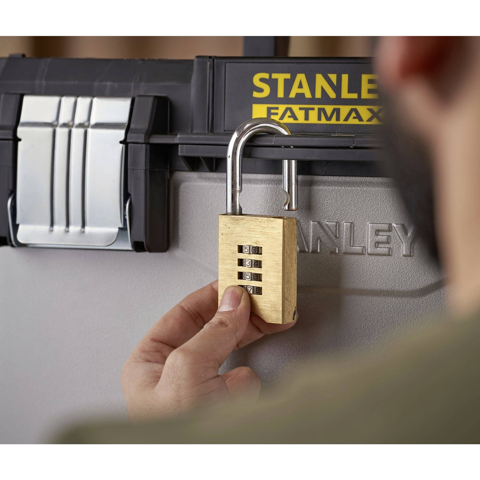 Visací zámek je otevírán osobou na šedém boxu s nápisem "Stanley Fatmax".