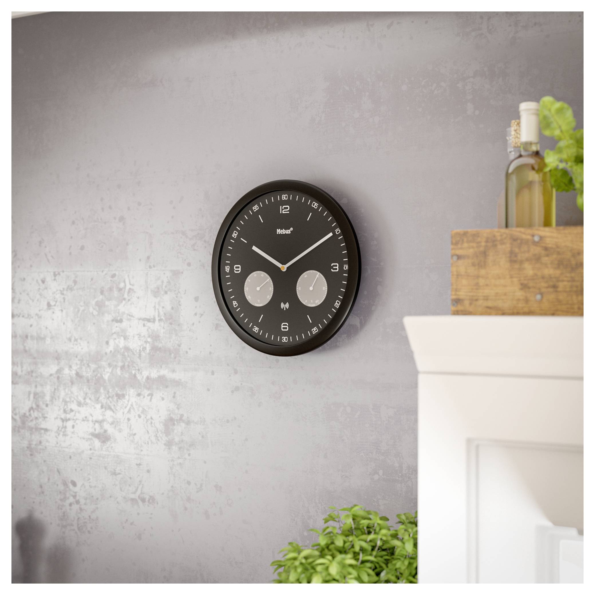 Nástennné hodiny s čiernym rámom a dvoma menšími ciferníkmi, ktoré zobrazujú miestny aj medzinárodný čas, visia na textúrovanej sivej stene.