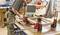 Remeselník upevňuje drevený rám pomocou svoriek na pracovnom stole v dielni. V pozadí sú viditeľné nástroje a materiály.