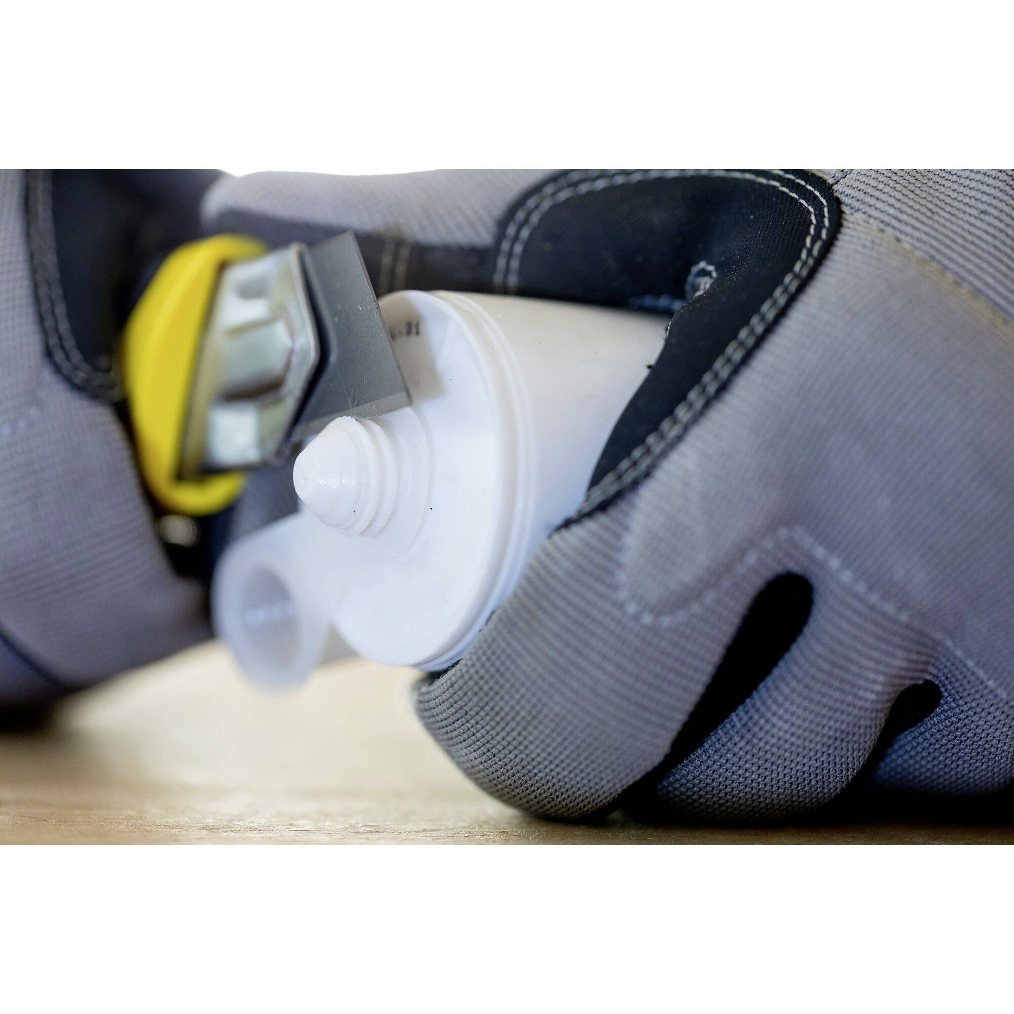 Osoba v šedých rukaviciach drží otvorenú bielu trubičku lepidla a žltý nástroj.