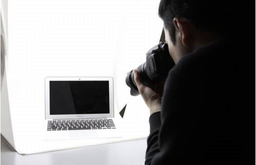 Osoba fotografuje laptop v bielom fotografickom štúdiu. Laptop je umiestnený pred svetlým pozadím.