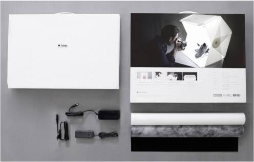 Fotografické štúdio-set: úložný box, fotograf vedľa mini-fotostúdia s osvetlenou obuvou, dva napájacie zdroje, pozadie na rolke.