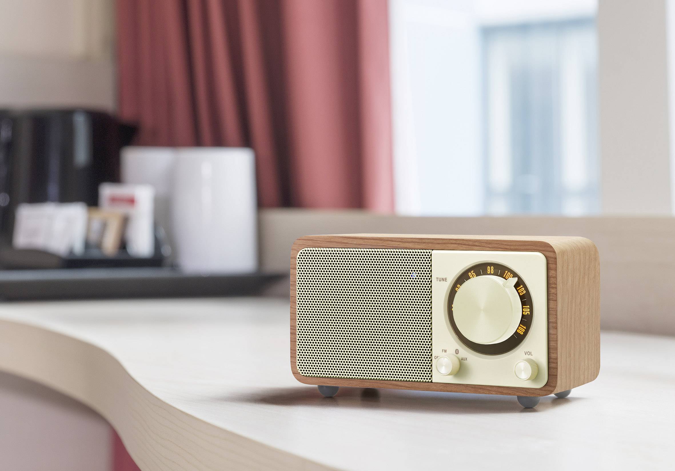 Retro rádio stojí zapnuté na stole v štýlovej miestnosti so červenými závesmi a modernými bytovými doplnkami.