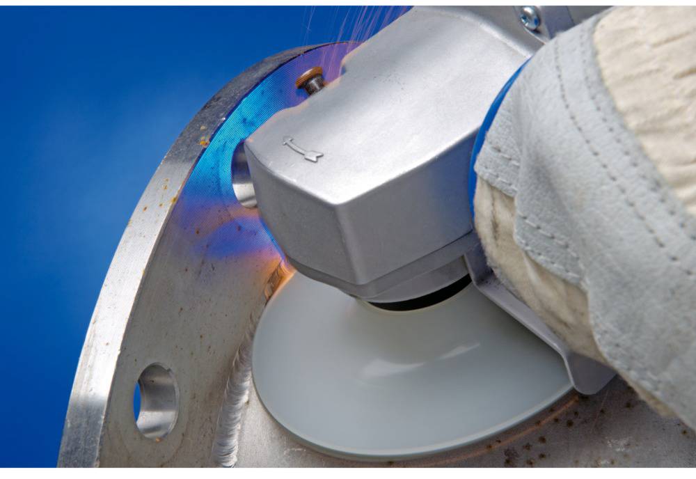 Osoba brúsi kovovú plochu uhlovou brúskou. Iskry lietajú a ostré hrany sa vyhladzujú.