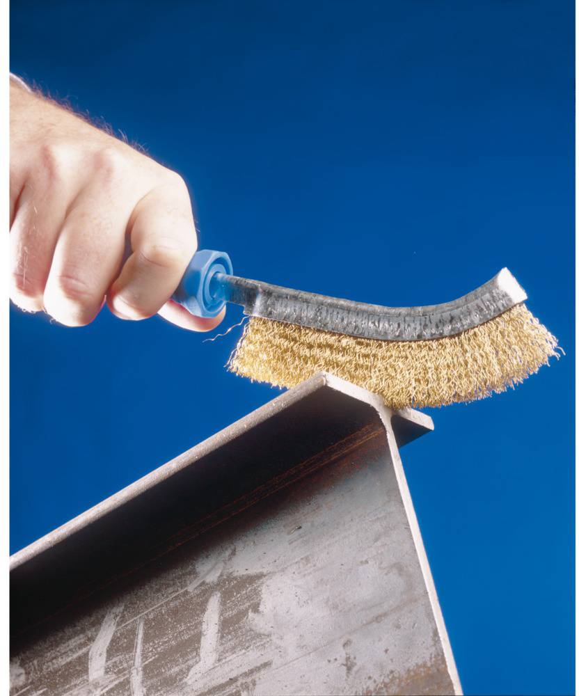 Ruka čistí kovový profil malou drôtenou kefou pred modrým pozadím.