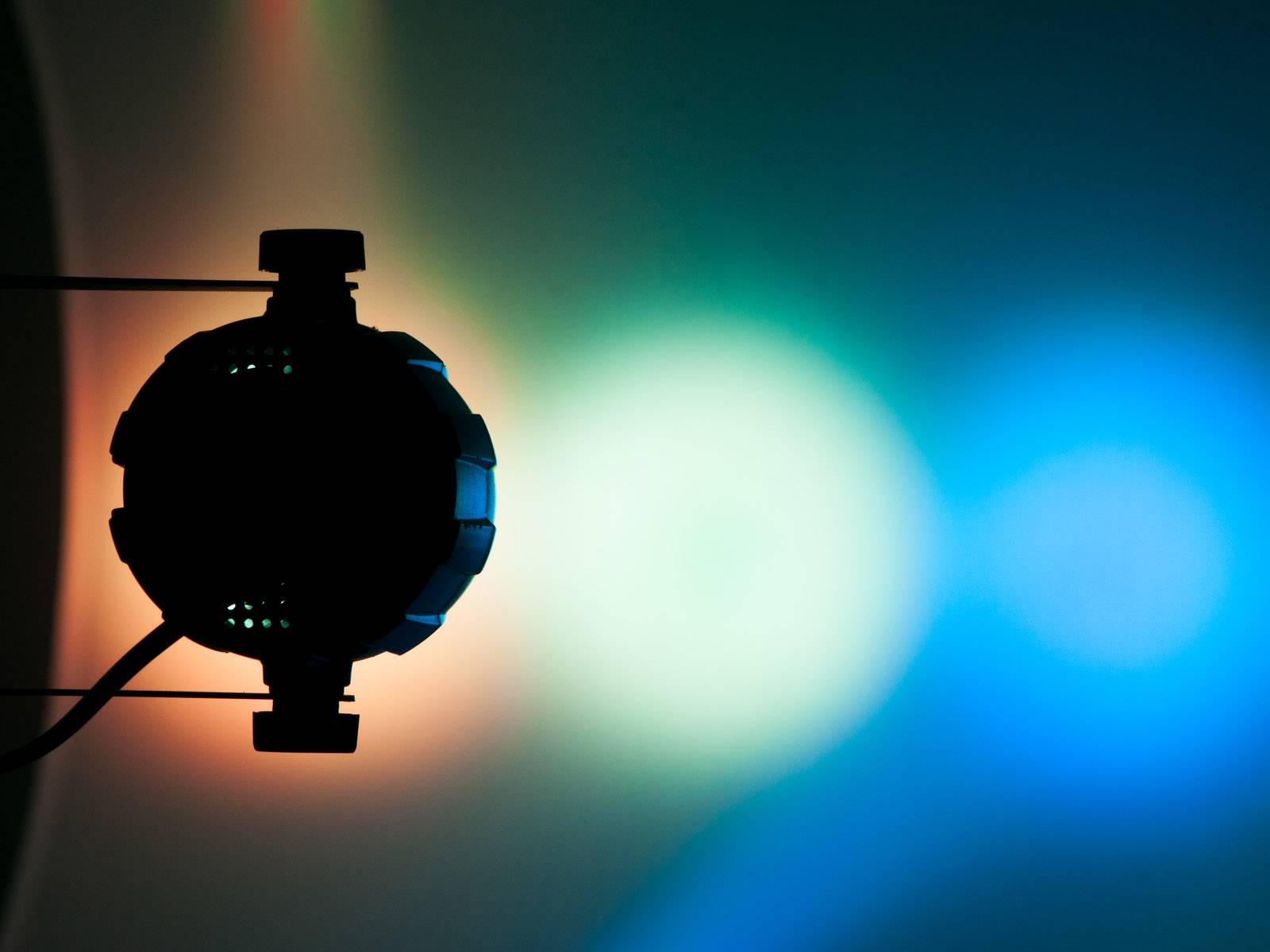 Tmavý objekt pred pozadím, ktoré sa ligotá farbami červenou, zelenou a modrou od ľavej strany smerom doprava.