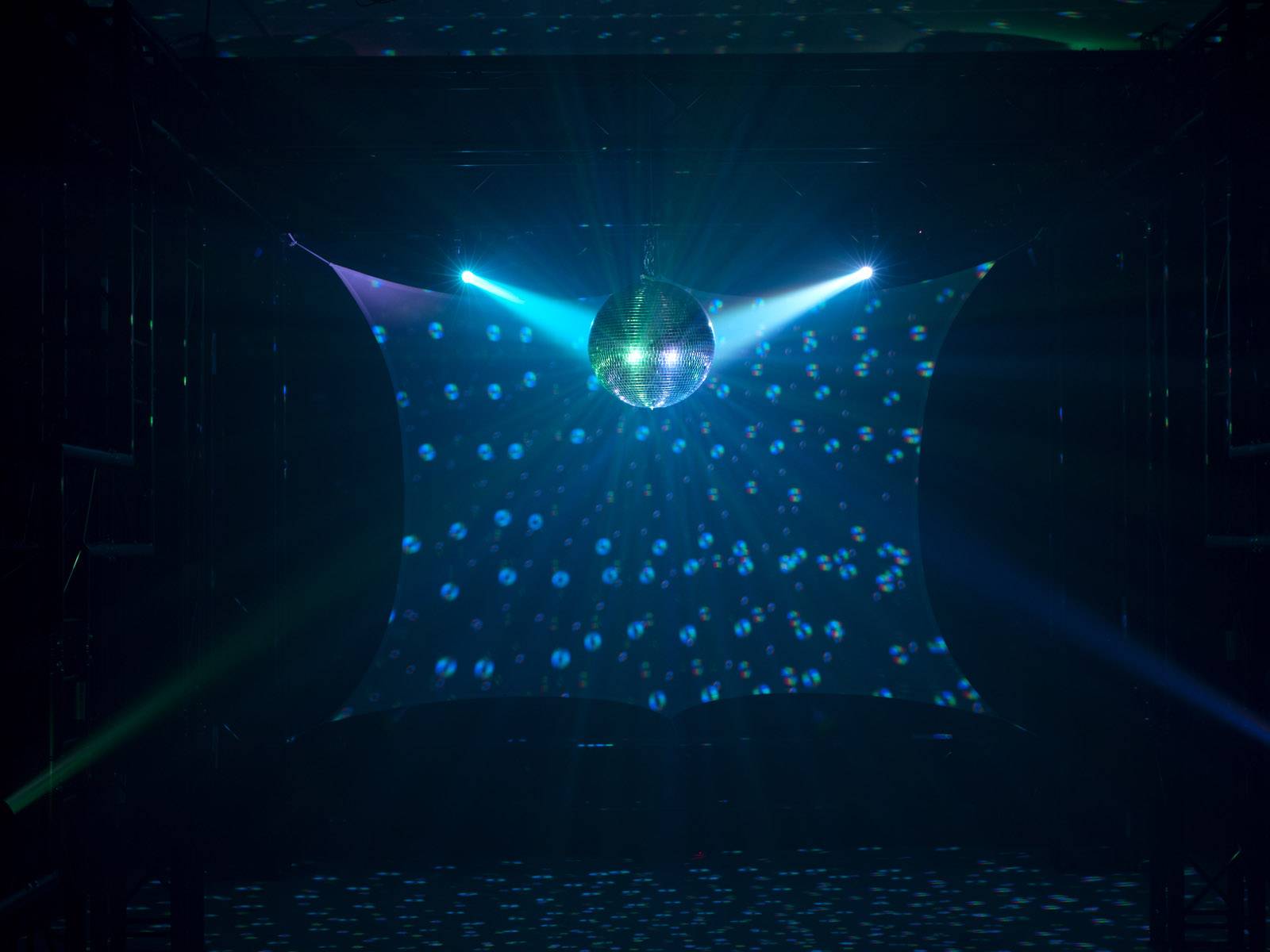 Trblietavá diskotéková guľa visí zo stropu, osvetlená modrými reflektormi, ktoré vytvárajú žiarivé svetelné efekty v priestore.