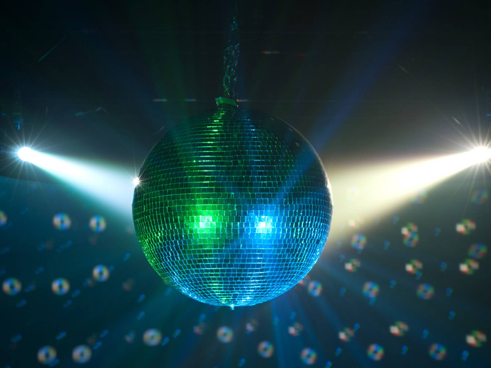 Disco guľa visí zo stropu a odráža pestré svetlá v tmavej miestnosti, čím vytvára živú párty atmosféru.