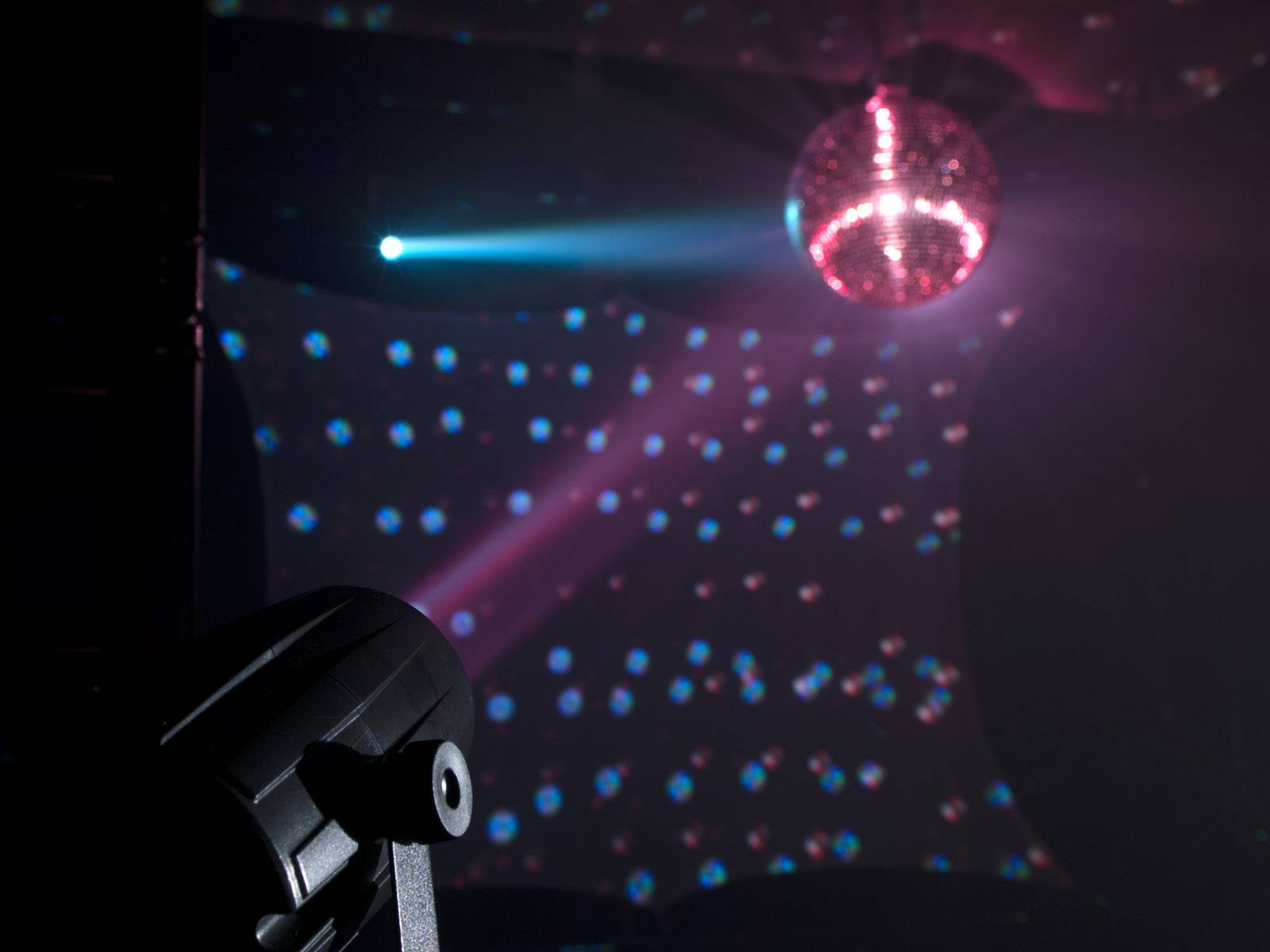 Miestnosť s diskotékovou guľou na strope, ktorá odráža pestrofarebné svetlá. Reflektor vyžaruje modré svetlo.