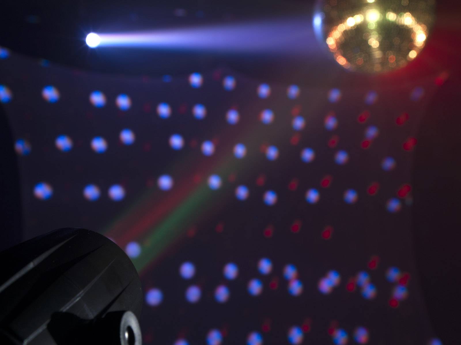 Diskokeguľa v tmavej miestnosti premieta pestré svetelné body na steny. Svetelný lúč reflektora svieti zľava.