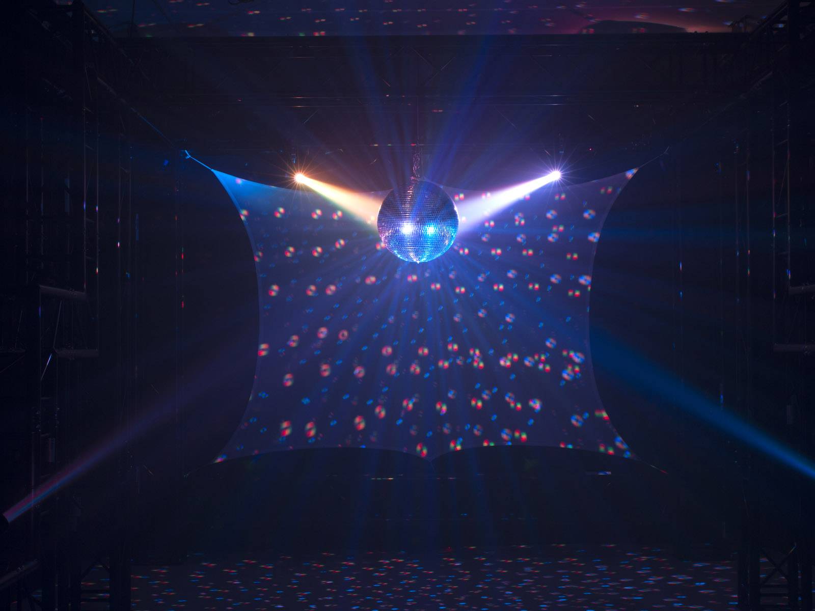 Diskokguľa v tmavom priestore, osvetlená dvoma svetelnými lúčmi, vytvára vzor farebných svetiel na plátne a podlahe.
