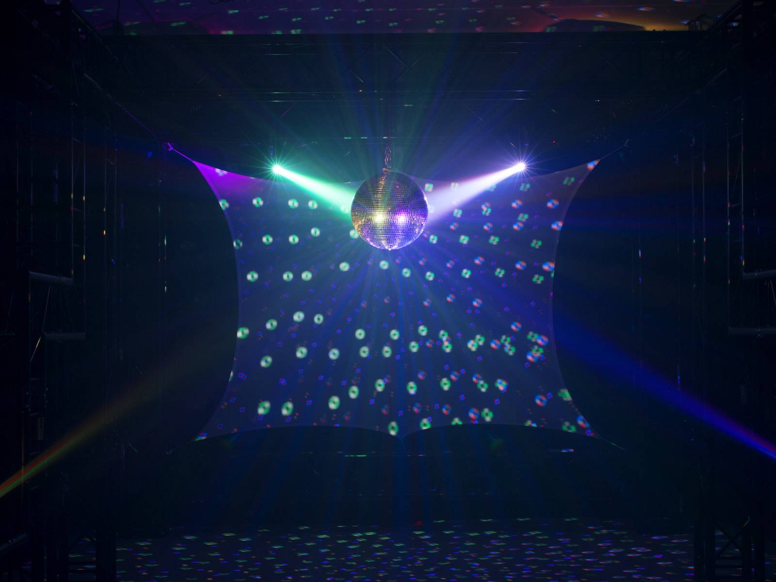 Disco guľa visí v priestore, odráža pestré svetlá na tanečnom parkete. Tmavé prostredie, atmosféra plná nálady.