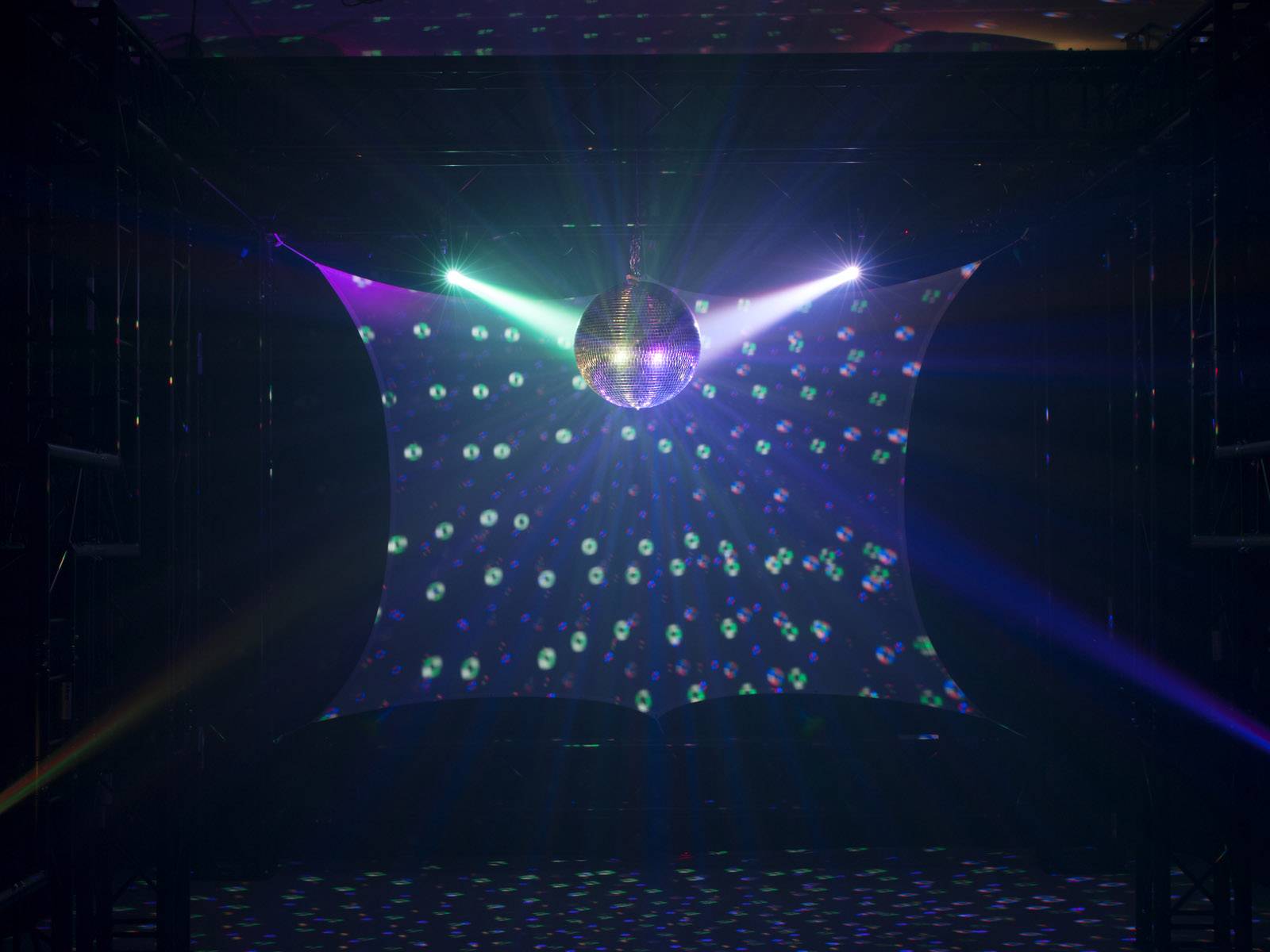Diskotanečná guľa v tmavom priestore vrháva pestrofarebné svetelné lúče a vzory na steny, vytvára živú tanečnú atmosféru.