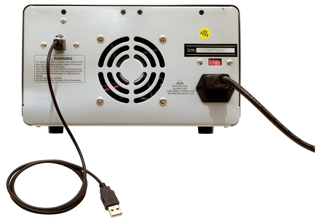 Zadná strana elektronického zariadenia s vetracou mriežkou, káblovými prípojkami a USB káblom; viditeľné výstražné upozornenia a sériové číslo.