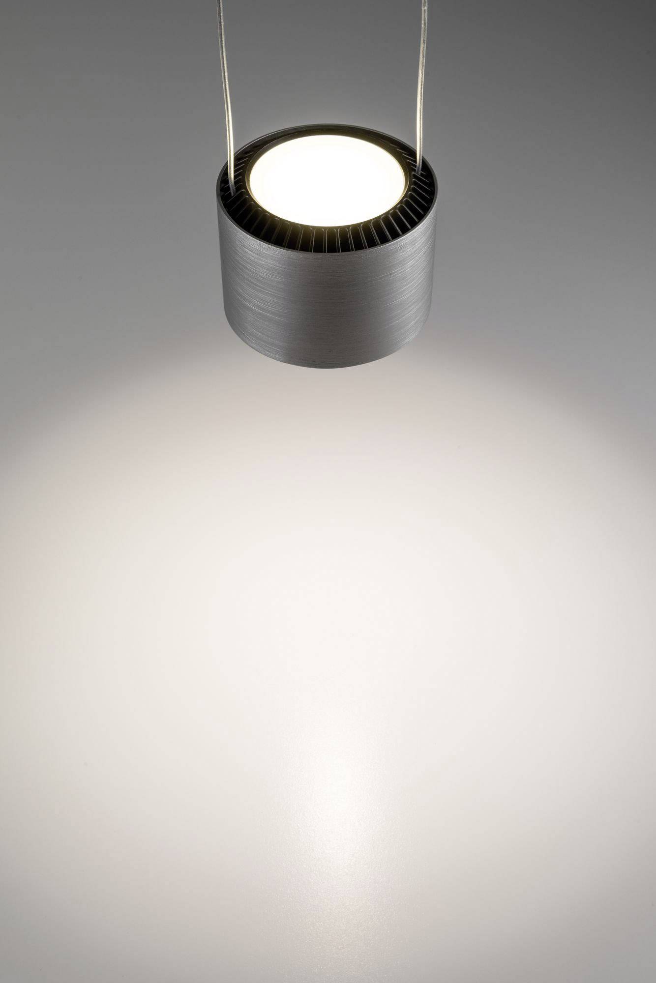 Moderná stropná lampa so strieborným krytom visí zo stropu a vyžaruje jasné svetlo na šedý povrch pod ňou.