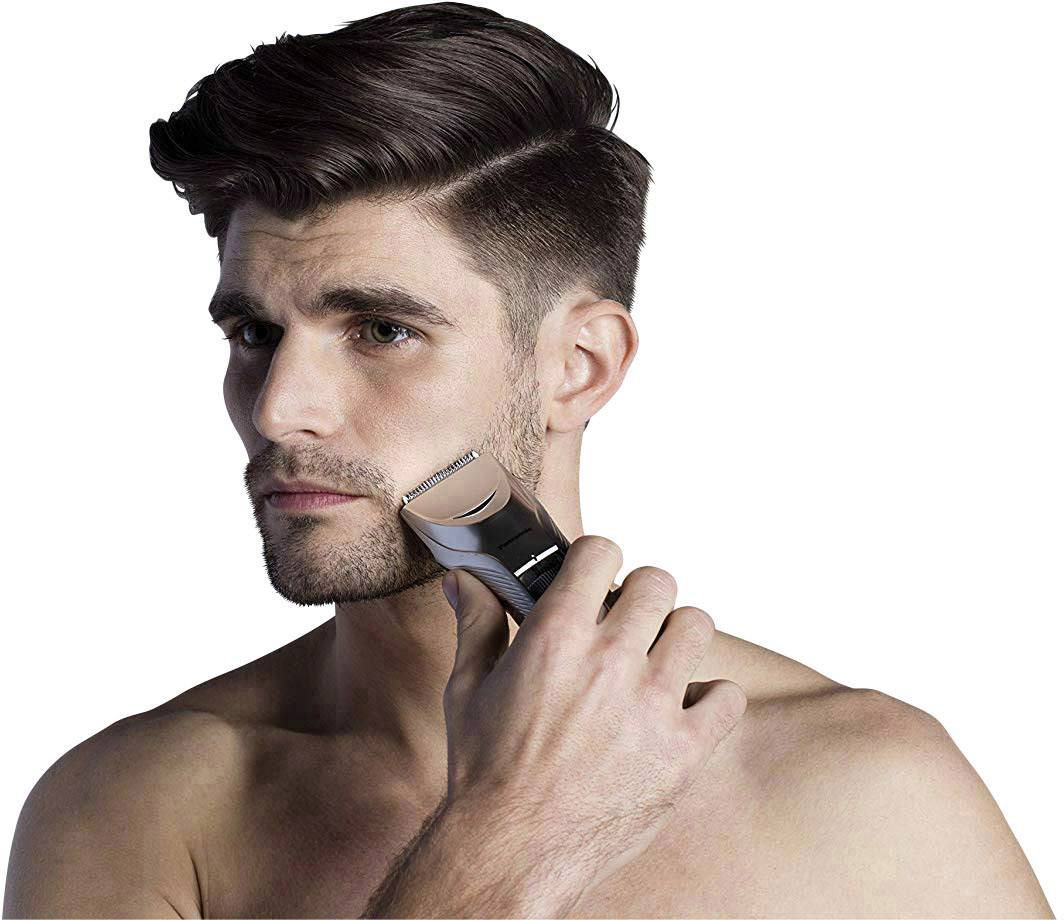 Muž si holí tvár elektrickým holiaceho strojčekom. Má tmavé, krátke vlasy a pozadie je biele.