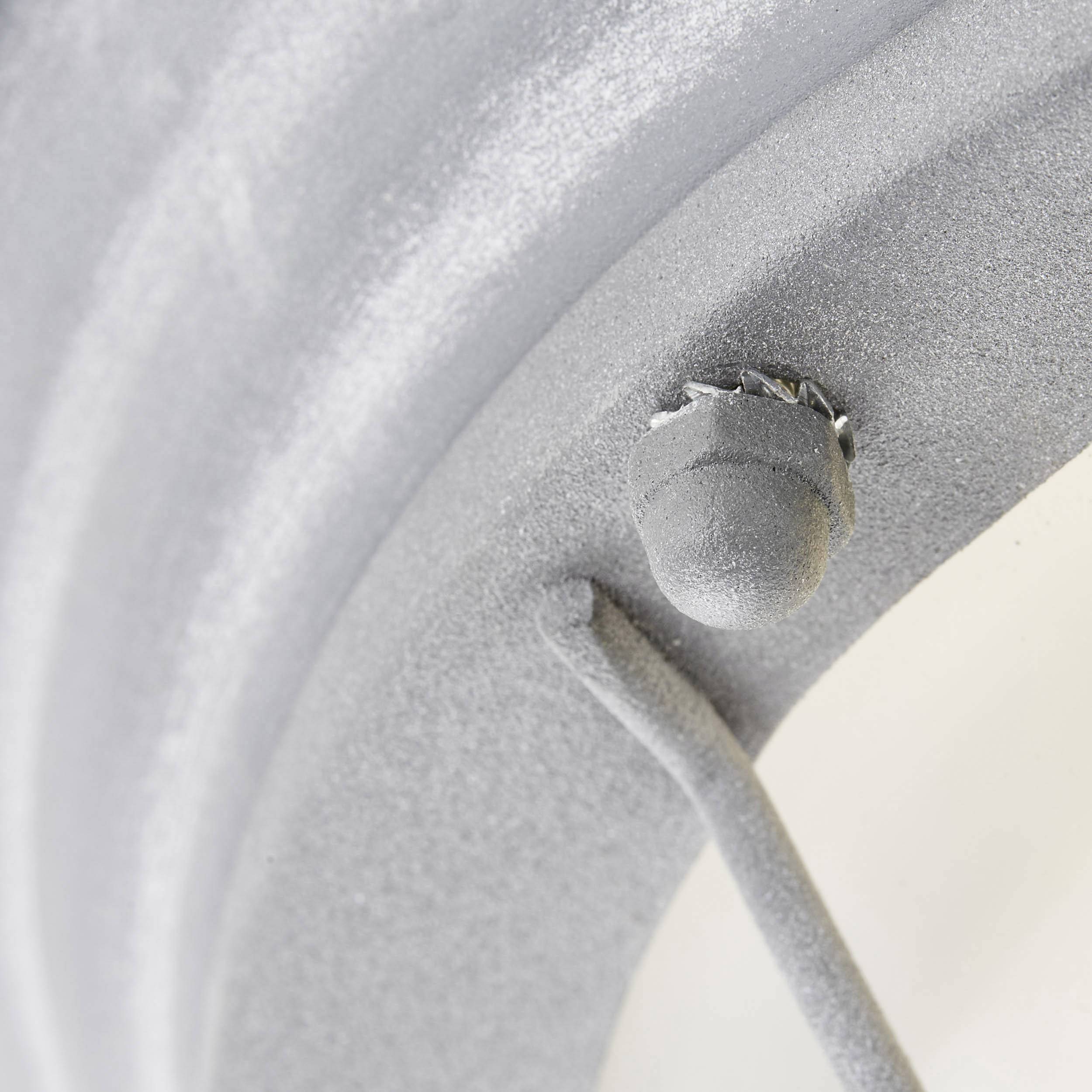 Detailný záber bielo nalakovaného, zaobľeného kovového povrchu s malým vyčnievajúcim gombíkom. Jednoduché, priemyselné dizajnové riešenie.