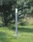 Moderná strieborná vonkajšia lampa stojí na zelenej trávnatej ploche, obklopená stromami v pozadí.