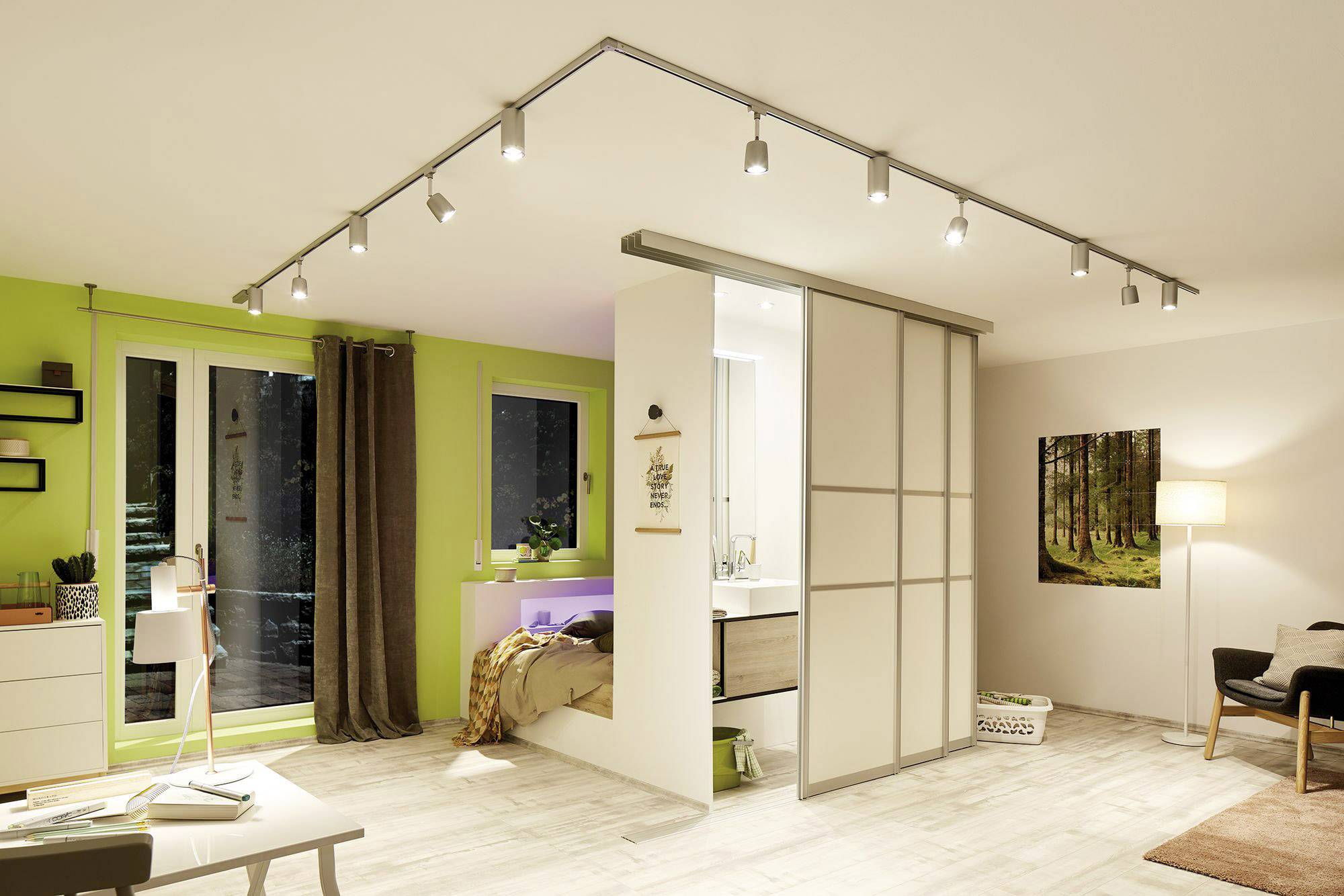 Moderná obývačka s pracovným stolom v ľavom rohu, so svetlým dôrazom na zelené a biele steny a štýlovým osvetlením. Spálňa oddelená posuvnými dverami.