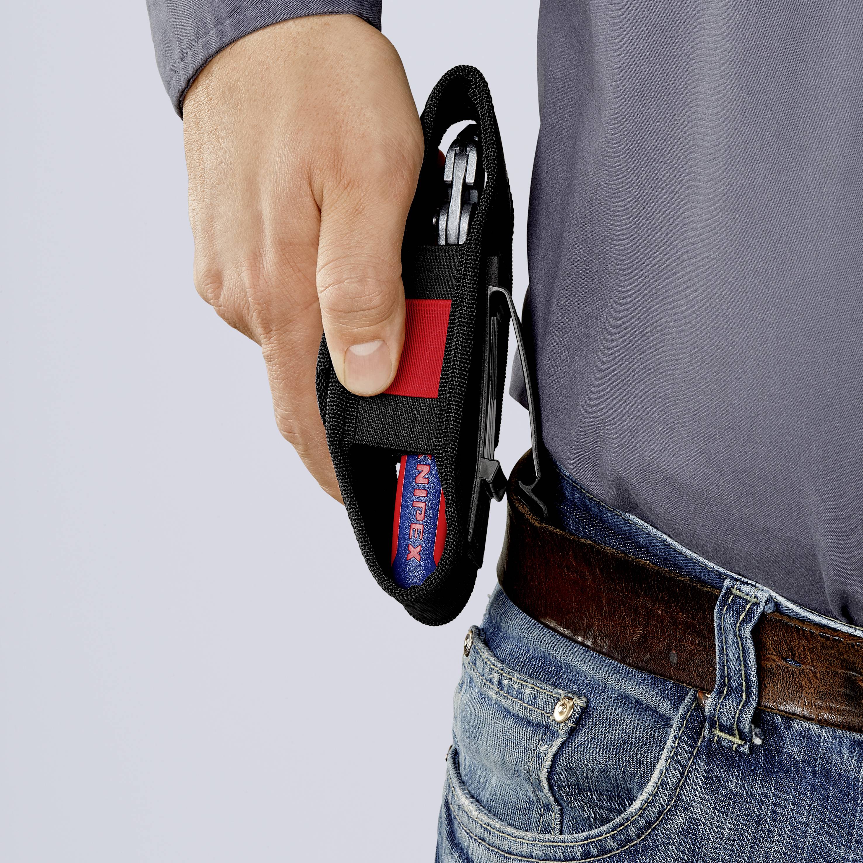 Osoba vyťahuje kliešte na drôty z červenej tašky pripevnenej na opasku. Kliešte sú čiastočne viditeľné a ich rukoväť je červená.