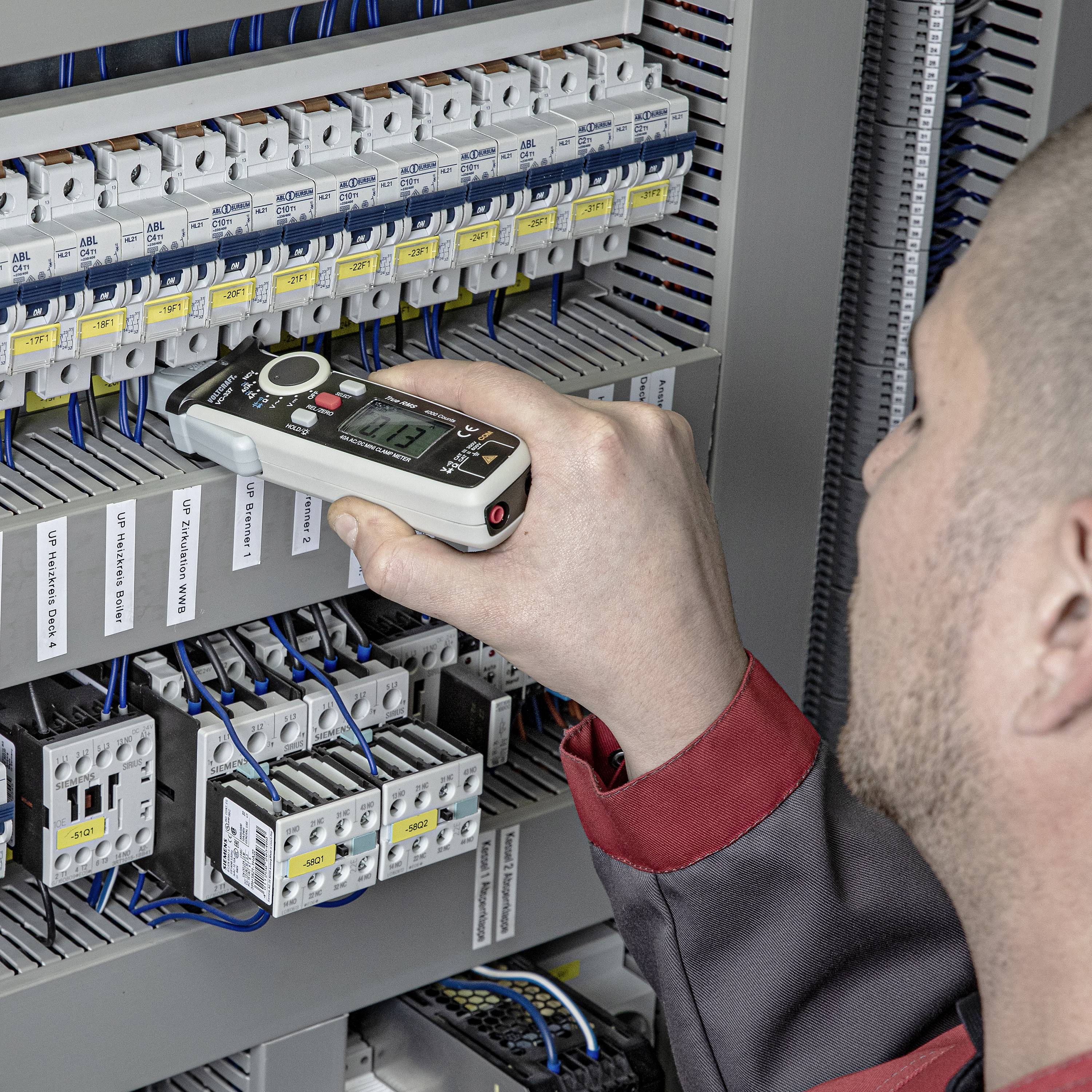 Osoba kontroluje elektrickú rozvádzač pomocou digitálneho meracieho prístroja za účelom merania napätia elektrických obvodov.