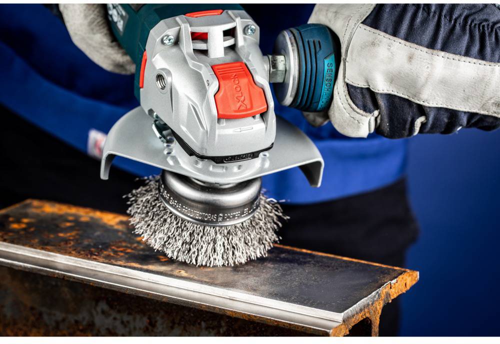 Osoba používa elektrické brúsne zariadenie s drôtenou kefou, aby odstránila hrdzu z kovového predmetu.