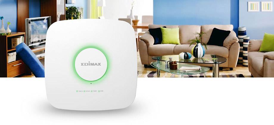 Na stolíku v obývacej izbe stojí Wi-Fi router. V pozadí sú viditeľné televízor, pohovka a dekorácie.