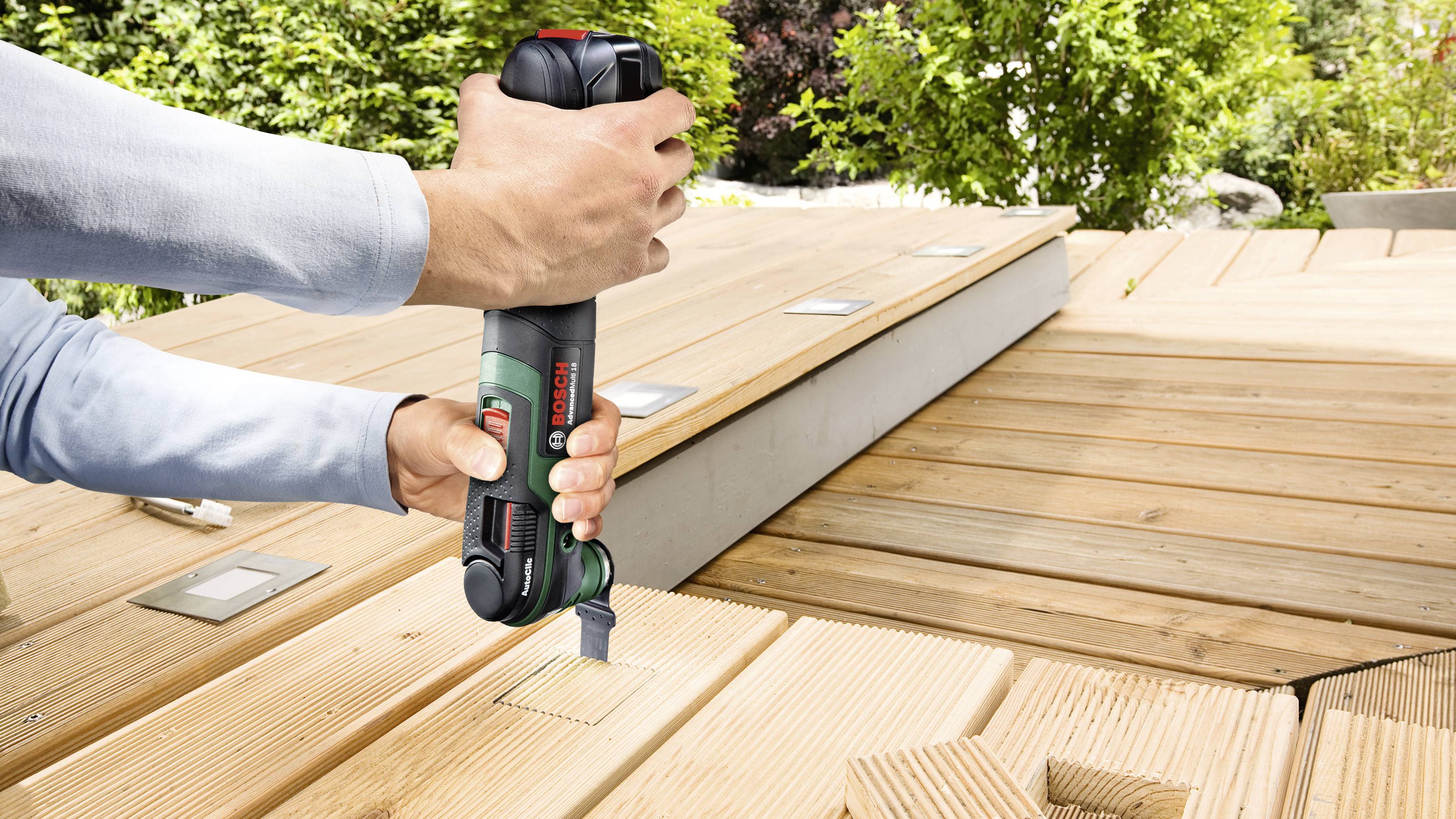 Osoba používa elektrický nástroj na vyvŕtanie diery do drevenej terasy. Nástroj je držaný šikmo, aby zabezpečil presnosť.