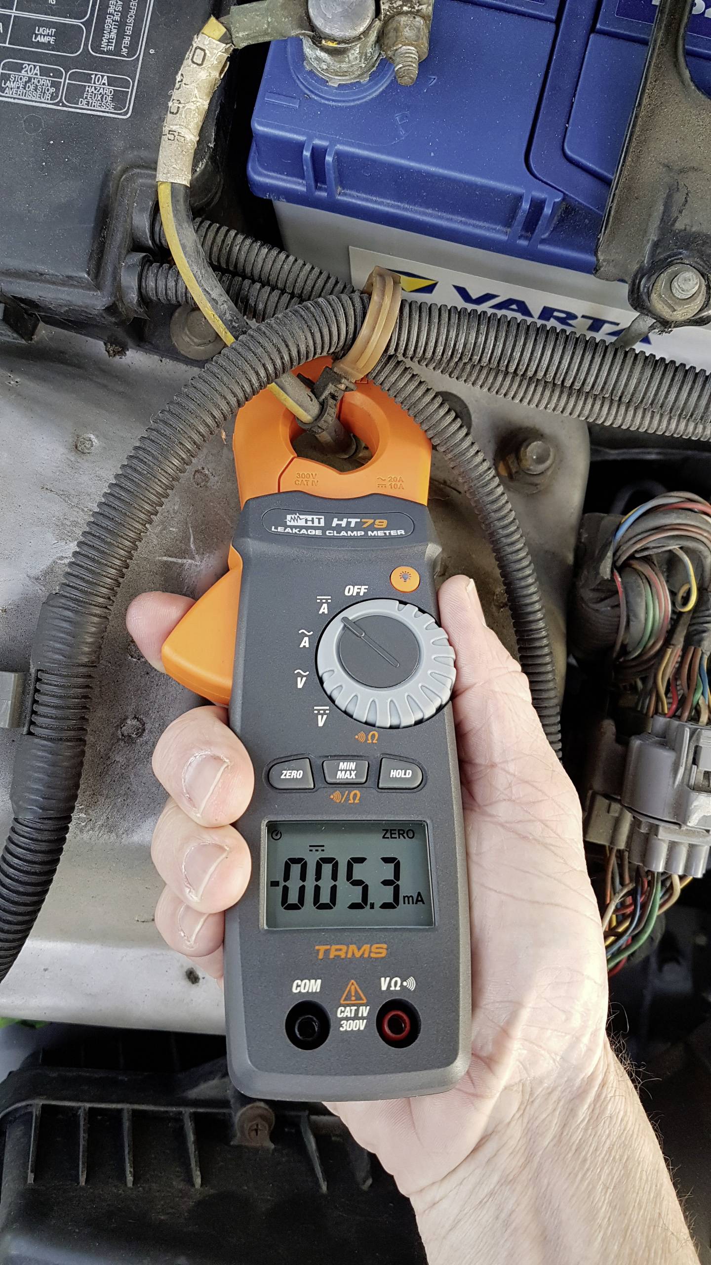 Multimeter ukazuje prúdové meranie 5,3 mA na napájacom kábli automobilu. Osoba drží prístroj na kábli v blízkosti batérie.