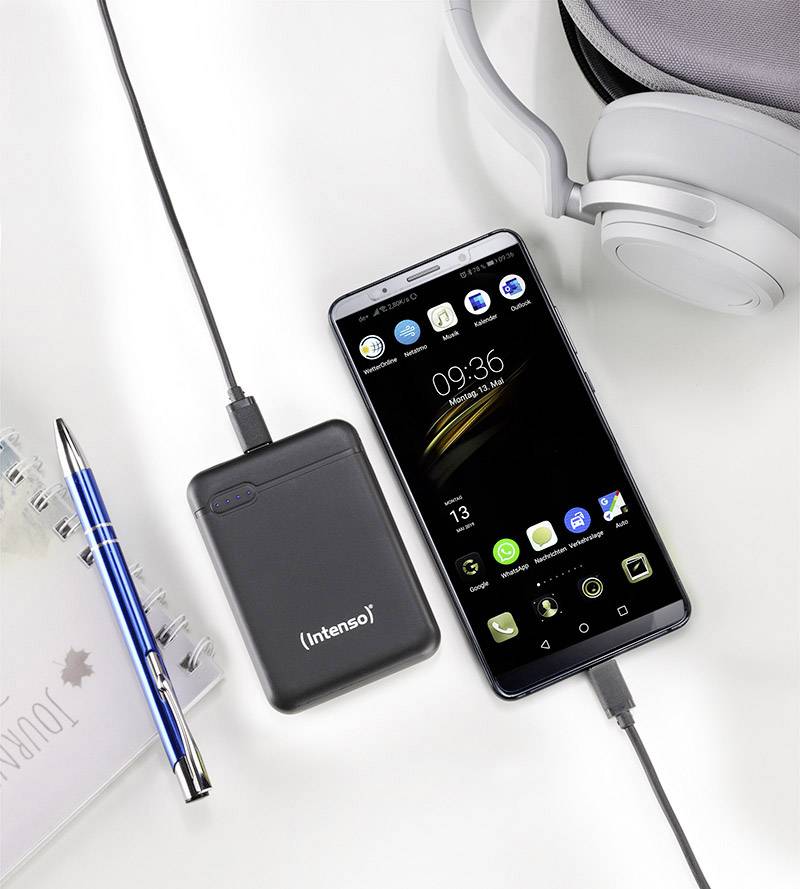 Smartfón sa nabíja z externej powerbabanky. Vedľa ležia modrý pero, notes a slúchadlá.