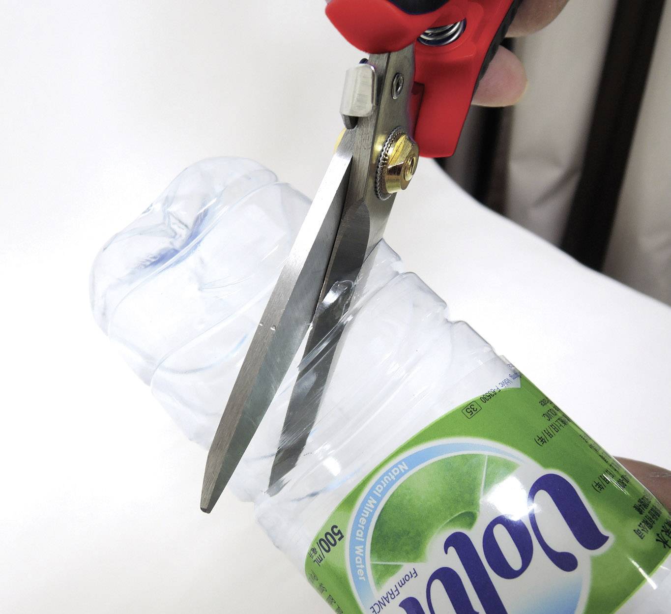 Jedna osoba strihá plastovú fľašu nožnicami. Hlavné body: Recyklácia a kreatívne využitie odpadu.